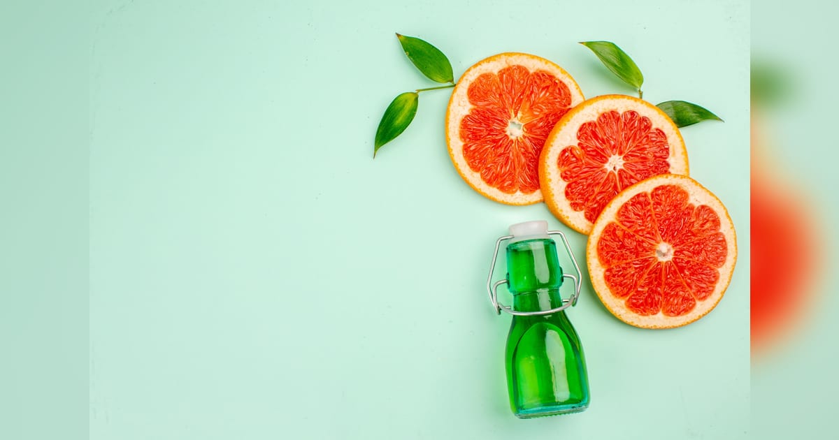 Frasco verde com fatias de grapefruit em fundo verde-claro.